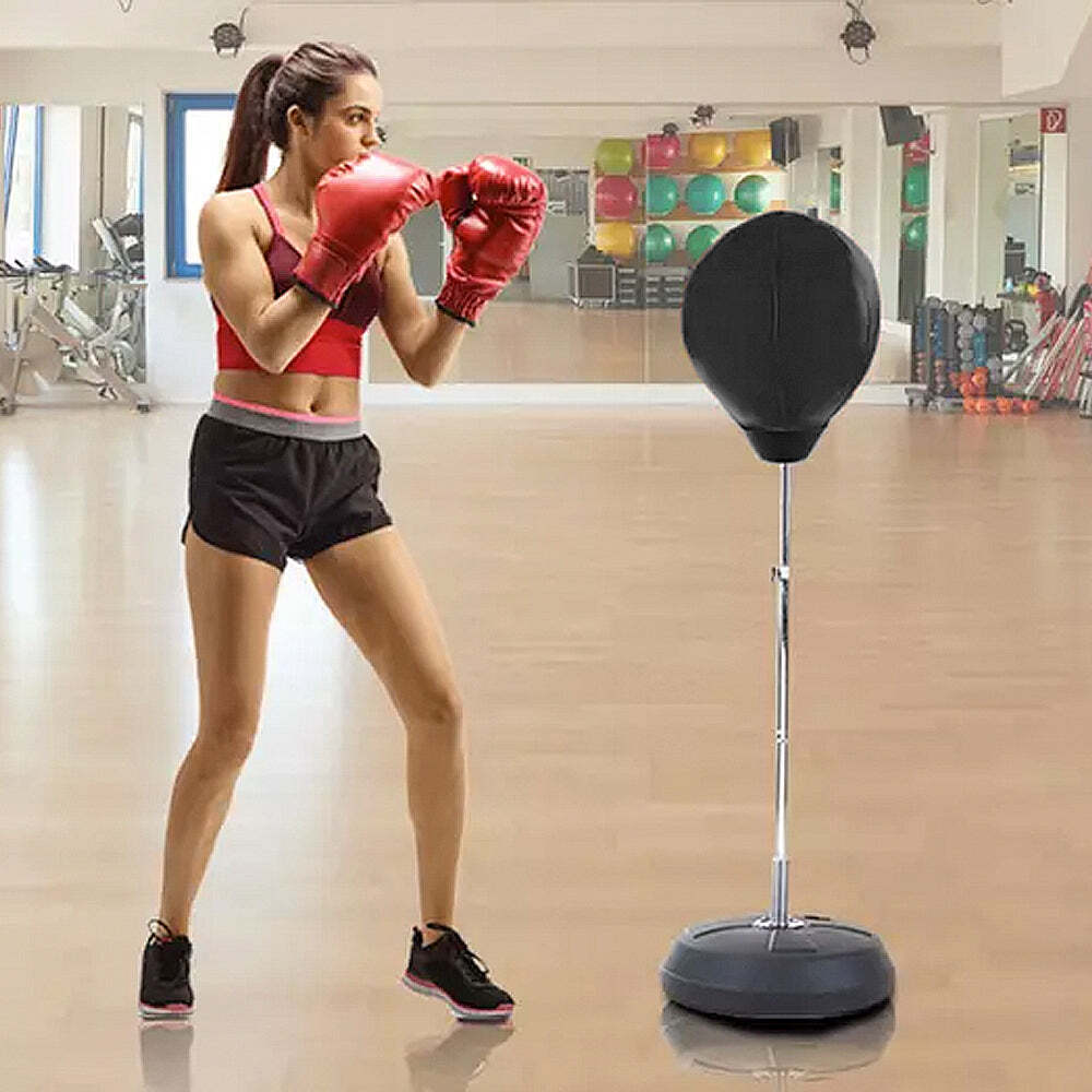 Woman in a gym wearing red boxing gloves and black shorts, standing next to a black punching bag.