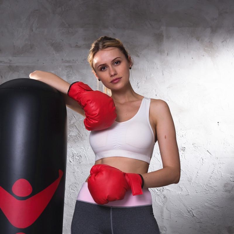 Woman in red boxing gloves posing next to a punching bag against a textured wall.