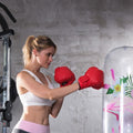 Woman in athletic wear and red boxing gloves punching a colorful punching bag against a gray wall.