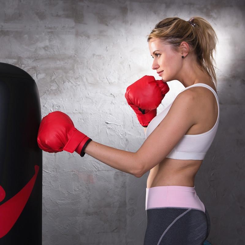 Woman in red boxing gloves training with a punching bag against a gray wall.