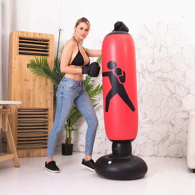 Woman in red boxing gloves standing next to a black inflatable punching bag with a red figure on a white floor.