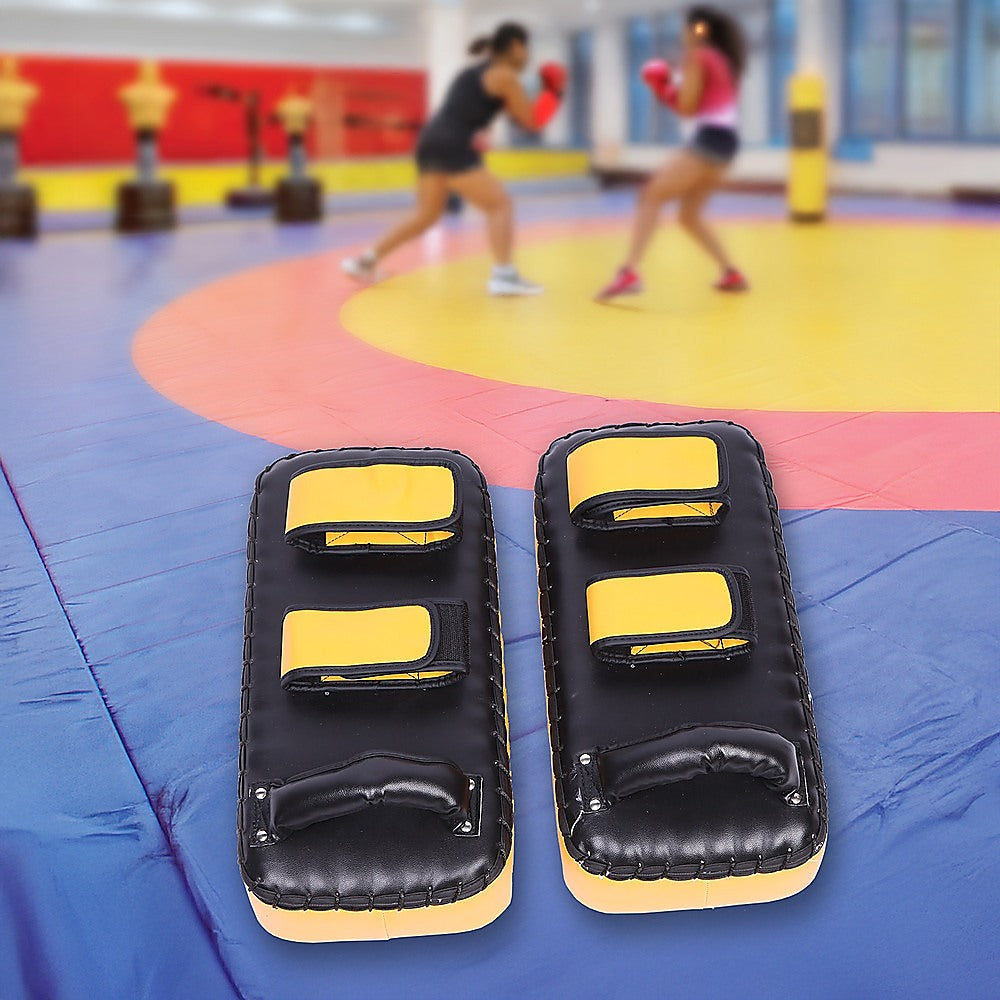 Pair of black and yellow boxing pads on a colorful mat with blurred background of people exercising.