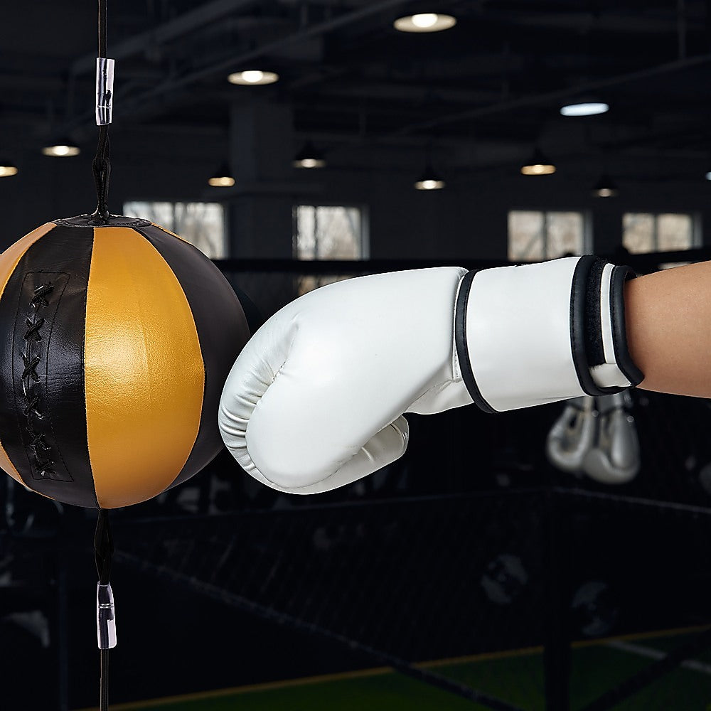 Person wearing a white boxing glove hitting a black and orange punching bag in a gym.